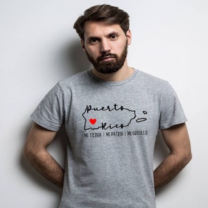 Puede incluir: Una camiseta gris con un contorno negro de Puerto Rico y las palabras "Puerto Rico" y "Mi tierra, mi patria, mi orgullo". Un coraz&oacute;n rojo est&aacute; dentro del contorno de Puerto Rico.