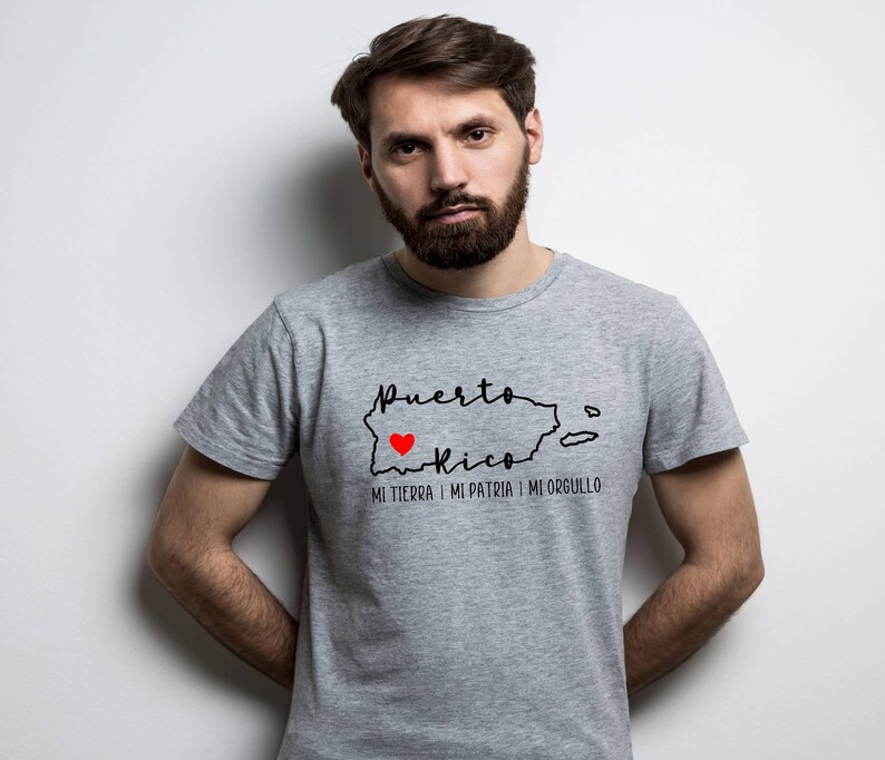 Puede incluir: Una camiseta gris con un contorno negro de Puerto Rico y las palabras "Puerto Rico" y "Mi tierra, mi patria, mi orgullo". Un coraz&oacute;n rojo est&aacute; dentro del contorno de Puerto Rico.