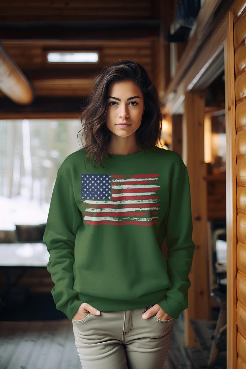 May include: A green sweatshirt featuring a distressed American flag design. The flag has a blue field with white stars and red and white stripes. The sweatshirt is worn by a person with dark hair.