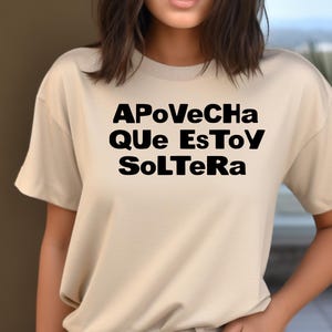 May include: Beige short-sleeved t-shirt with the phrase "APoVeCHa QUE EsToY SoLTeRa" printed in black. The text is centered on the front of the shirt. The shirt is made of a soft material.