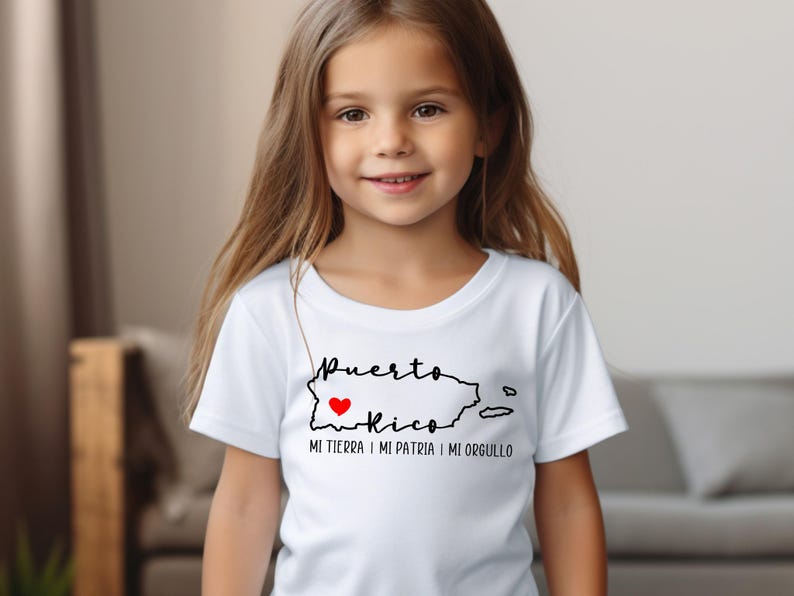 Puede incluir: Una camiseta blanca con un contorno negro de Puerto Rico y las palabras "Puerto Rico" con un coraz&oacute;n rojo en el medio. El texto debajo del contorno dice "Mi tierra, mi patria, mi orgullo."