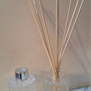 May include: Two clear glass bottles with textured surfaces, one filled with a liquid and the other with wooden sticks. The bottles have silver caps.