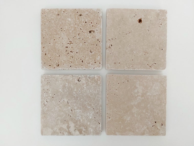 Op de afbeelding: Vier vierkante beige travertijn tegels met een ruw, getextureerd oppervlak.