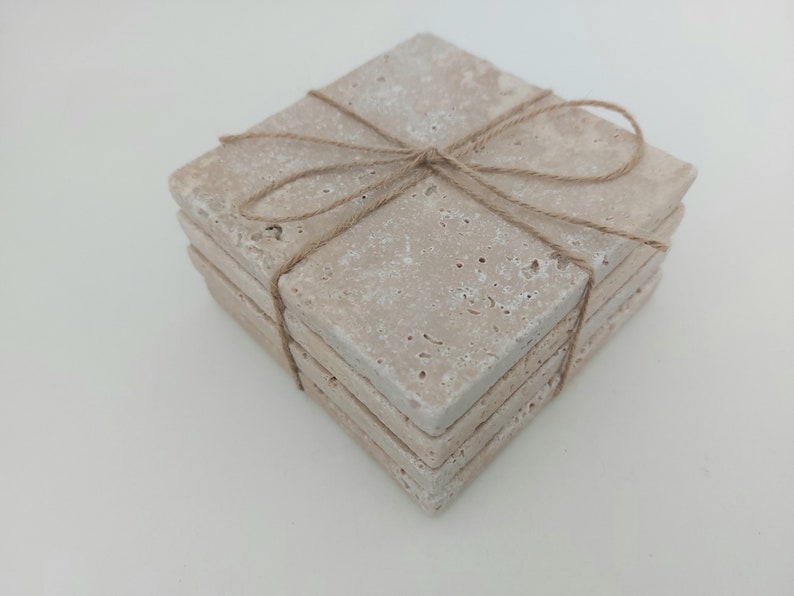 Op de afbeelding: Set van vier beige stenen onderzetters die met touw aan elkaar zijn gebonden. De onderzetters hebben een ruw, getextureerd oppervlak.