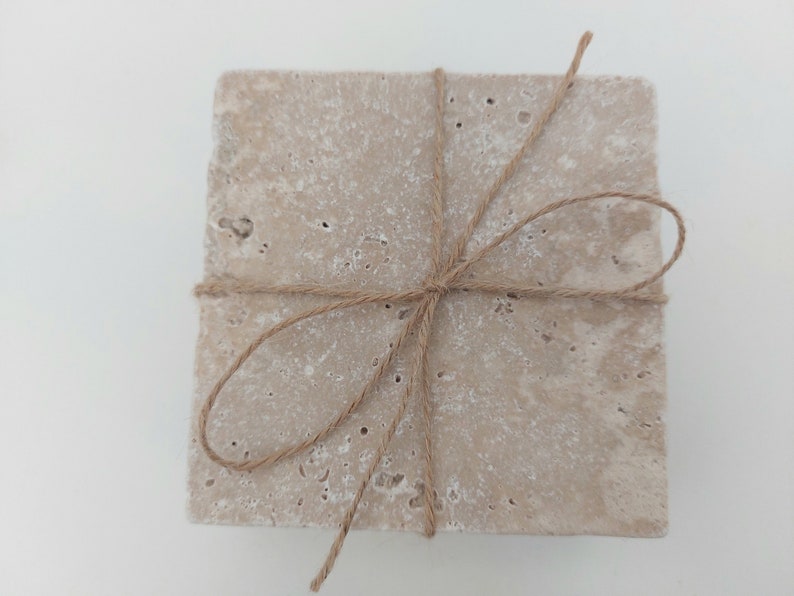 Op de afbeelding: Set van vier beige stenen onderzetters die met touw aan elkaar zijn gebonden. De onderzetters hebben een ruw, getextureerd oppervlak.