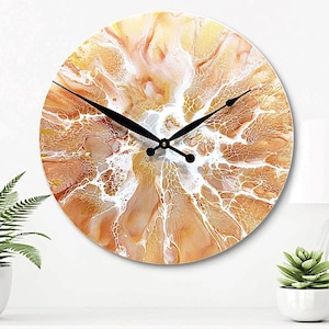 May include: A round wall clock with a white and gold abstract design. The clock has black hands and a white face.