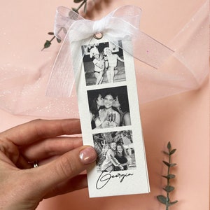Bookmark style photo card strip in black and white. Features 3 personalised photos and name on the front. The back says will you be my bridesmaid or maid of honour.Tied with a white organa bow.