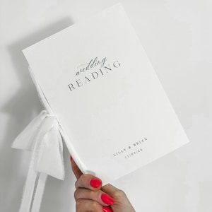 May include: A white wedding reading booklet with the words "wedding READING" printed in dark blue script. The names "LILLY & BRIAN" and the date "11/04/26" are printed in a smaller font. A white ribbon is tied to the booklet.