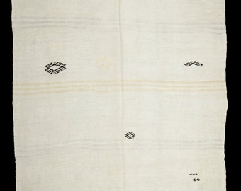 Può includere: Una coperta bianca tessuta con disegni geometrici neri e il testo "COLCA" e "S" ricamato su di essa.