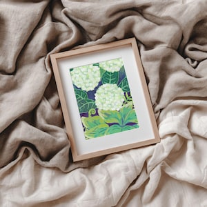 May include: A rectangular wooden frame containing a print of white hydrangea flowers with green leaves against a dark blue background. The artwork features a botanical illustration style with visible brushstrokes and vibrant green foliage.