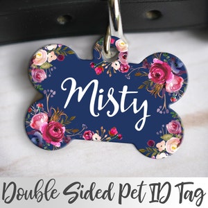 Puede incluir: Etiqueta de identificación para mascotas de doble cara en forma de hueso con fondo azul marino y diseño floral. La etiqueta tiene el nombre "Misty" escrito en letra cursiva blanca.
