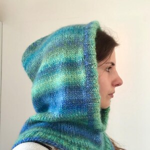 May include: A hand-knitted hood in a variegated yarn featuring shades of teal, blue, and lime green. The hood has a thick, ribbed border around the face opening and covers the head and neck, constructed with a chunky knit texture throughout.