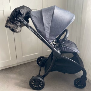 May include: A black stroller with a gray fabric seat and canopy. The stroller has a black handle with a fur-lined hand muff. The handle has the text "@furcoatonnappiesforjones" printed on it.
