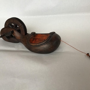 May include: A vintage wooden chalk line reel. The reel is dark brown with an orange interior and a small wheel. A thin orange string extends from the reel, ending with a small nail. This tool is used for marking straight lines.