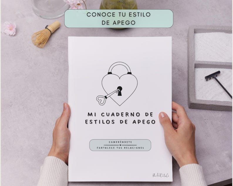 A white notebook with the text "MI CUADERNO DE ESTILOS DE APEGO" and the phrases "CONOCE TU ESTILO DE APEGO" and "COMPRENDETE FORTALECE TUS RELACIONES". The cover features a heart-shaped lock and key design.