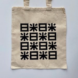 Peut inclure: Un sac fourre-tout beige avec un motif noir de carrés répétés contenant les caractères "米" et "日".