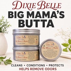 May include: Two stacked silver metal tins of Dixie Belle Big Mama's Butta in Orange Grove and Suzanne's Garden scents, each 10 oz, beside a 4 oz tin of Unscented Big Mama's Butta. Labels include instructions, Made in USA, and Eco Friendly text.