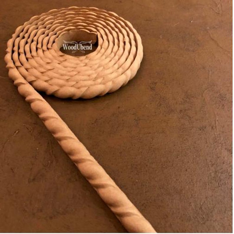 May include: A coiled, light brown wooden trim with a spiral design, and the text "WoodUbend" in the center. The trim is on a brown surface.