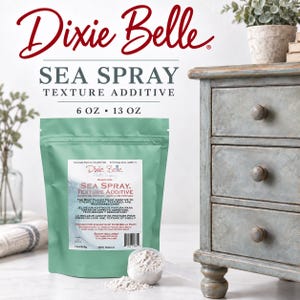 May include: A light green pouch of Dixie Belle Sea Spray texture additive with white label text. The label reads Sea Spray Texture Additive and 13 oz/368g. A small white scoop filled with white powder sits in front of the pouch on a white surface.