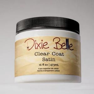 Może przedstawiać: Biały plastikowy słoik z czarną zakrętką zawierający Dixie Belle Clear Coat Satin. Etykieta zawiera nazwę marki, rodzaj produktu oraz objętość 473mL wydrukowaną czarnym tekstem na beżowym tle z ikoną pędzla.