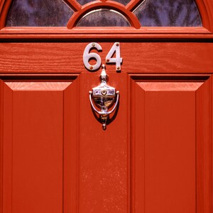 K&ouml;nnte beinhalten: Eine rote Haust&uuml;r mit einem silbernen T&uuml;rklopfer und der Nummer 64 darauf.