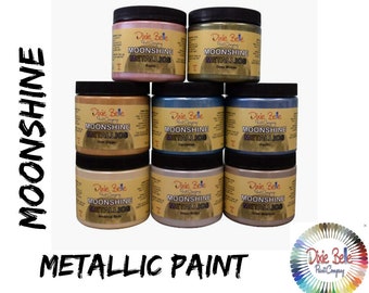 Puede incluir: Nueve botes de pintura metálica Moonshine Metallic de Dixie Belle en varios colores metálicos. Los botes están dispuestos en forma de pirámide. Los colores son: Rusty Rose, Deep Whipple, Gold Digger, Caribbean, Pacific, Wedding Cake, Silver Bullet, Steel Magnolia.