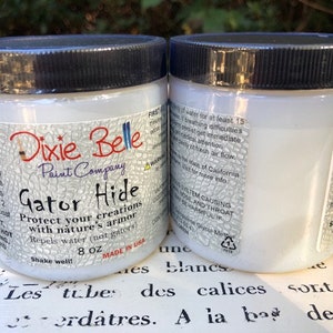 May include: Two white bottles of Dixie Belle Paint Company Gator Hide protectant. The bottles are labeled with the product name, company name, and instructions for use. The bottles are 8 ounces each.