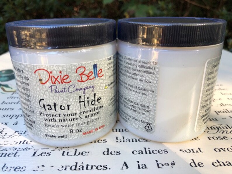 May include: Two white bottles of Dixie Belle Paint Company Gator Hide protectant. The bottles are labeled with the product name, company name, and instructions for use. The bottles are 8 ounces each.