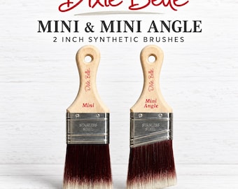 May include: Two 2-inch synthetic paint brushes by Dixie Belle, labeled Mini and Mini Angle. Each features a light wood handle with a hole, a stainless steel ferrule, and dark red bristles that fade to white at the tips for smooth coverage.