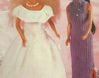 May include: Two dolls wearing knitted dresses. The doll on the left is wearing a white dress with a lace trim and a pearl necklace. The doll on the right is wearing a purple dress with a slit up the side.