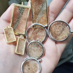 May include: A collection of eight gold and silver pendant charms with a variety of shapes and sizes. Each charm features a clear resin filled with a sparkly, glittery material.