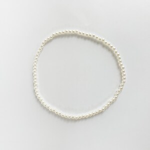 Puede incluir: Un delicado collar de perlas blancas, dispuesto en forma circular, descansa sobre un fondo blanco liso. El collar est&aacute; compuesto por numerosas perlas peque&ntilde;as y redondas, creando un aspecto cl&aacute;sico y elegante. Las perlas est&aacute;n espaciadas uniformemente.