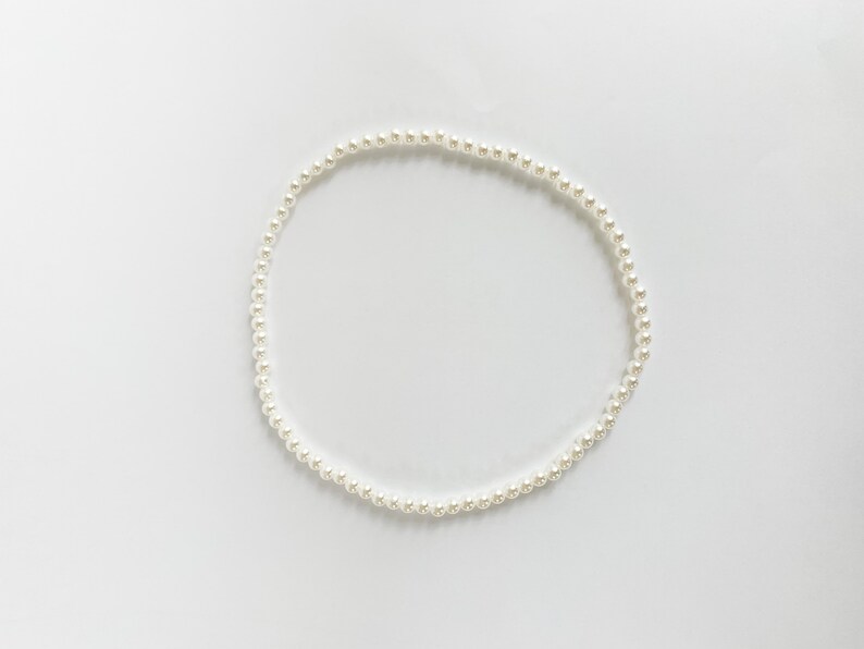 Puede incluir: Un delicado collar de perlas blancas, dispuesto en forma circular, descansa sobre un fondo blanco liso. El collar est&aacute; compuesto por numerosas perlas peque&ntilde;as y redondas, creando un aspecto cl&aacute;sico y elegante. Las perlas est&aacute;n espaciadas uniformemente.