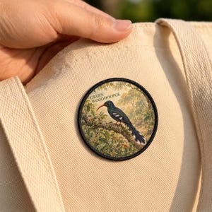 May include: A circular patch featuring a Green Woodhoopoe bird perched on a tree branch, attached to a beige canvas tote bag. The bird has dark plumage with white markings and a red beak. The text GREEN WOODHOOPOE is printed above the bird.