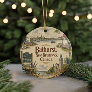May include: A round ceramic ornament featuring a scenic illustration of Bathurst, New Brunswick, Canada. The ornament includes a church, a gazebo, and a sign that says "Welcome to Bathurst". The ornament is suspended by a gold string.