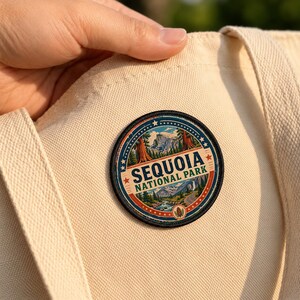 May include: A circular embroidered patch featuring a landscape illustration of Sequoia National Park with mountains, trees, and a river. The text 'SEQUOIA NATIONAL PARK' is printed in dark blue letters on a cream canvas tote bag fabric.