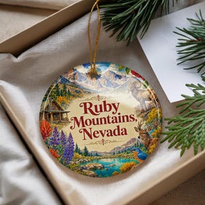 May include: A round ceramic ornament featuring a colorful landscape illustration of the Ruby Mountains, Nevada, with a cabin, bighorn sheep, deer, and blue bird. The text Ruby Mountains, Nevada is printed in dark red in the center with a gold string.