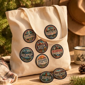 May include: A beige canvas tote bag decorated with five circular embroidered patches featuring colorful illustrations of Yellowstone, Yosemite, Zion, Redwood, and Saguaro National Parks. Two additional patches for Sequoia and Grand Canyon lie below.