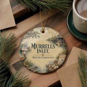May include: Round ceramic ornament featuring a scenic illustration of Murrells Inlet, South Carolina. The design includes boats, a pier, and the text "Murrells Inlet, South Carolina". A "Fresh Seafood" sign is also visible.