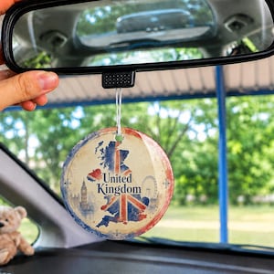 May include: A round car air freshener hanging from a rearview mirror, featuring a vintage-style map of the United Kingdom overlaid with the Union Jack flag, the text United Kingdom, and illustrations of Big Ben and the London Eye in blue and red.