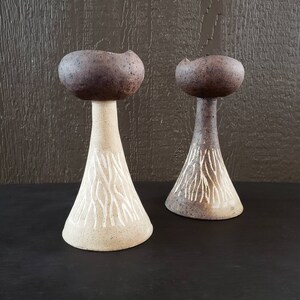 May include: Two ceramic candle holders with a brown and white striped design. The candle holders are shaped like mushrooms with a wide base and a narrow top.