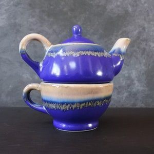 Peut inclure: Un ensemble théière et tasse en céramique bleu et crème. La théière a un couvercle et une poignée. La tasse a une poignée. L'ensemble a une finition émaillée avec un schéma de couleurs bleu et crème.