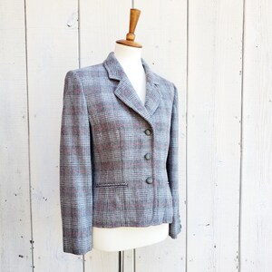 May include: A gray and pink plaid blazer with a single-breasted closure and three buttons. The blazer has a notched collar and a pocket on the left side.
