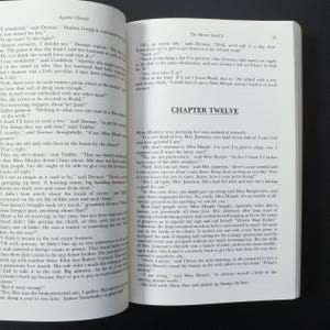 May include: Open book with text from Agatha Christie's "The Mirror Crack'd". The pages are yellowed, and the text is in black. Chapter Twelve is visible. The book is open on a dark surface.