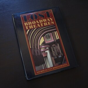 May include: A hardcover book titled "LOST BROADWAY THEATRES" by Nicholas Van Hoogstraten. The cover features a dark blue background with red and gold text and a detailed interior theater image. The book is on a dark surface.