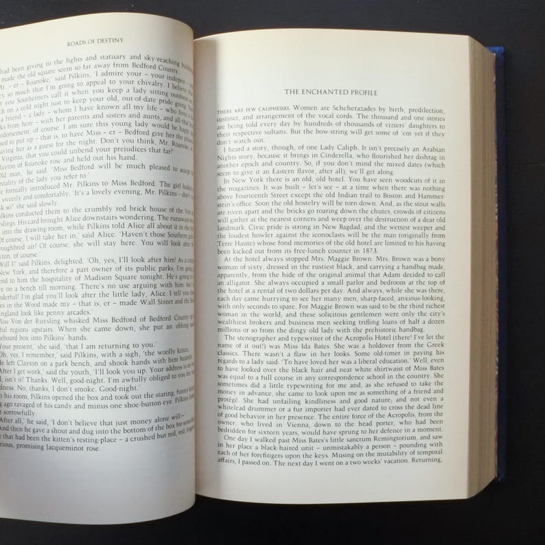 May include: Open book with text on the left page and a section titled "The Enchanted Profile" on the right. The pages are yellowed with age, suggesting an antique or vintage book.