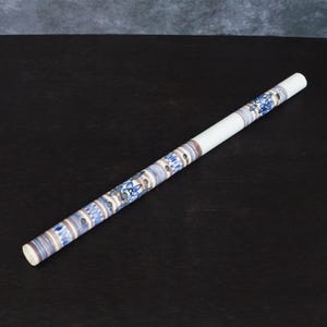 Peut inclure: Un repose-baguettes en céramique blanche avec une bande décorative ornée de motifs floraux et géométriques bleus. Le repose-baguettes est cylindrique et présente une finition lisse et brillante. Le design incorpore des nuances de bleu, de marron et de blanc.