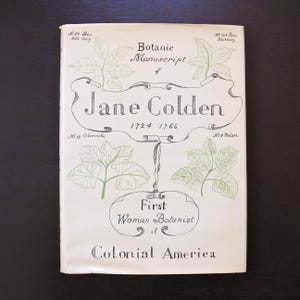 May include: A vintage book cover with the title "Botanic Manuscript of Jane Colden" and the years 1724-1766. The cover features botanical illustrations and the text "First Woman Botanist of Colonial America."