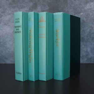 May include: A collection of hardcover books with teal covers and gold lettering. Titles include "Preserve and Protect," "Wuthering Heights," "The Instrument," and "Jane Eyre." The books are arranged vertically, with a black book on the right.