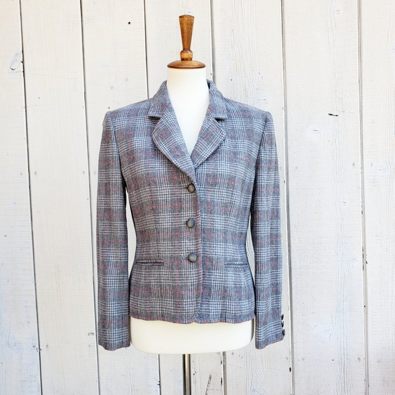 May include: A gray and pink plaid blazer with a notched collar and three buttons. The blazer has a fitted silhouette and long sleeves.